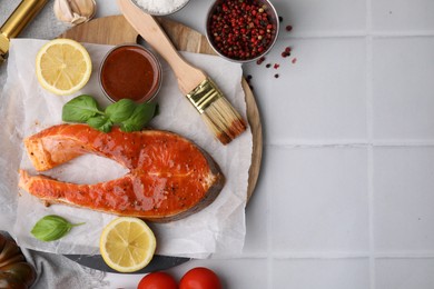 Photo of Fresh marinade, fish, lemon, brush and basil on white tiled table, flat lay. Space for text