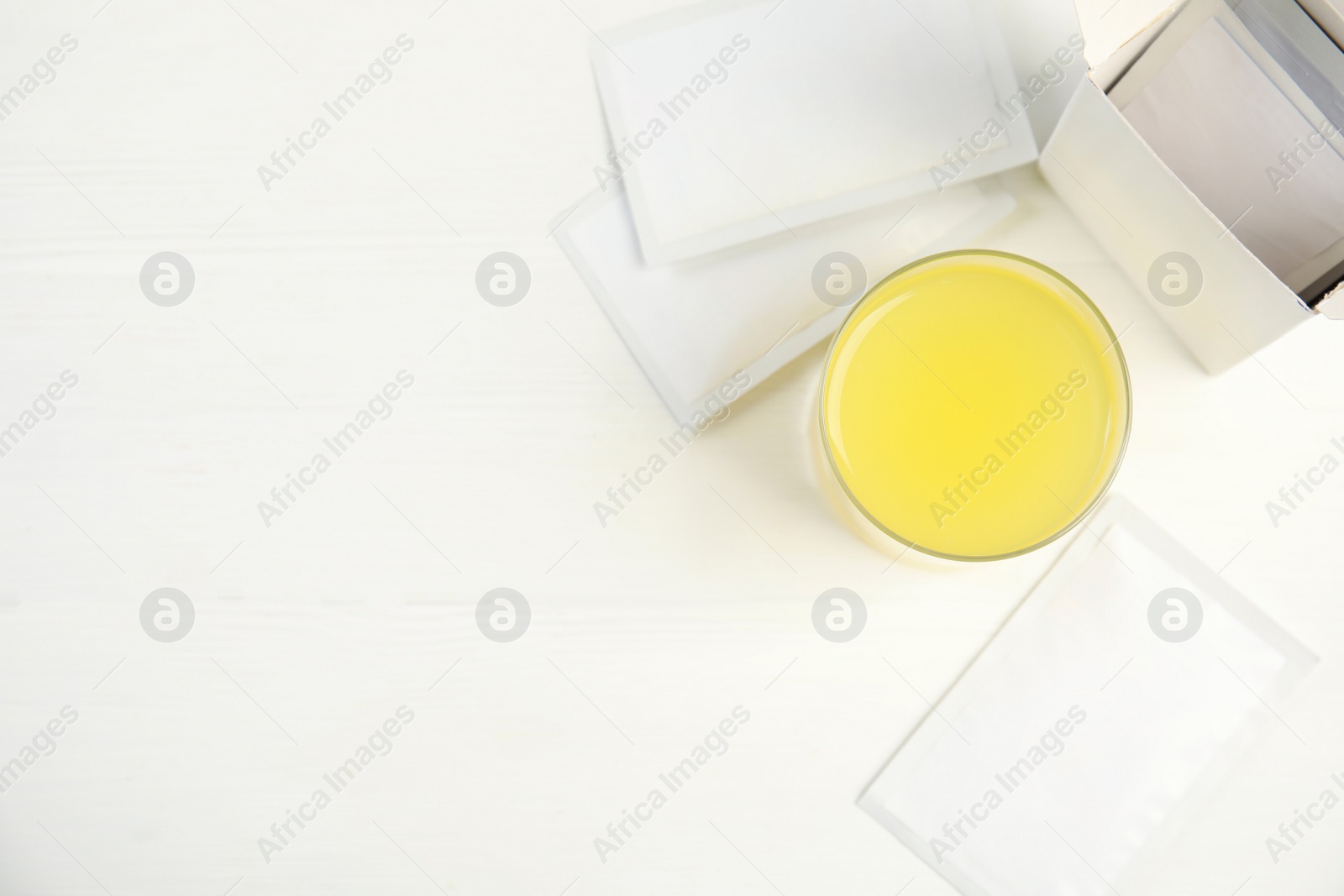 Photo of Medicine sachets and glass with dissolved drug on white table, flat lay. Space for text