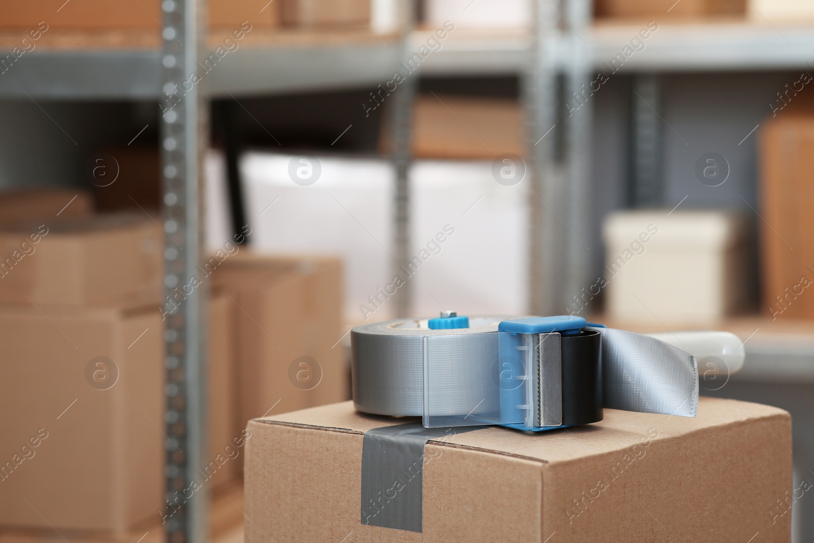 Photo of Adhesive tape dispenser on cardboard box indoors. Space for text