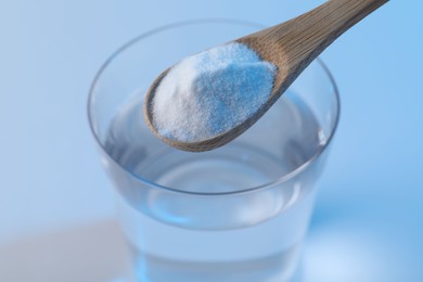 Photo of Spoon with baking soda over glass of water on light blue background, closeup