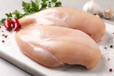 Photo of Raw chicken breasts and ingredients on light grey table, closeup