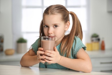 Photo of Cute little child drinking tasty chocolate milk in kitchen