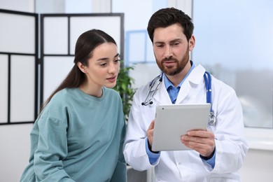 Photo of Doctor with tablet consulting patient during appointment in clinic