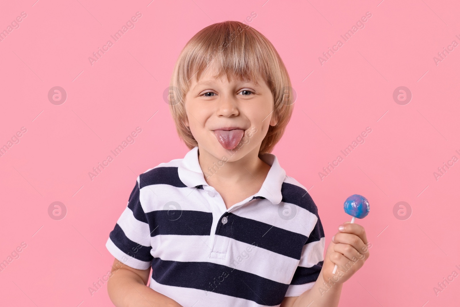 Photo of Funny little boy with lollipop showing tongue on pink background
