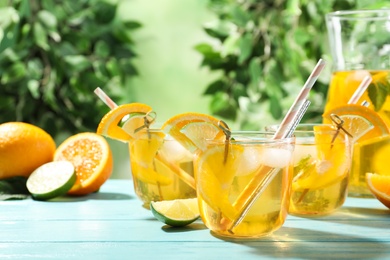 Delicious refreshing drink with orange and lime slices on light blue wooden table