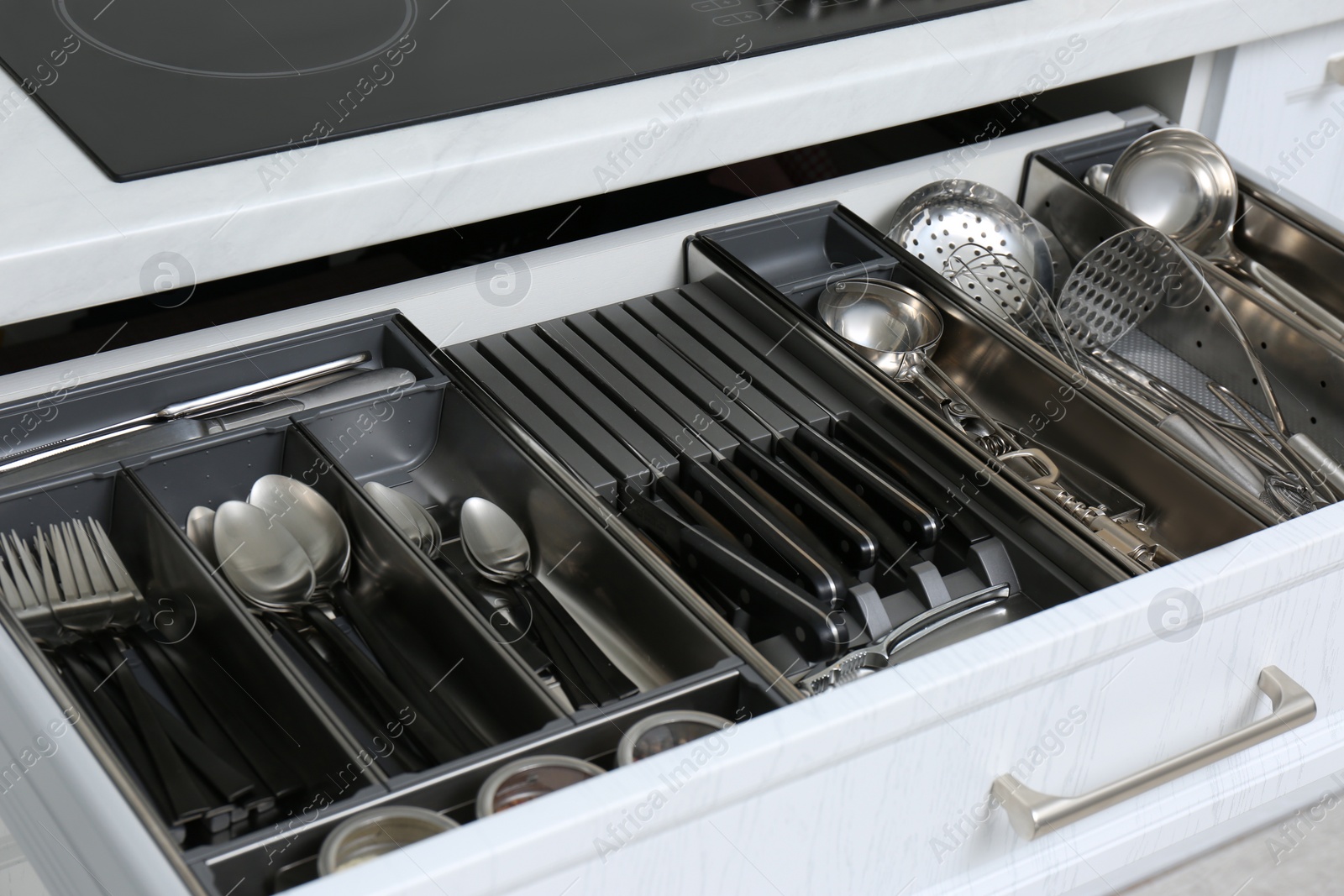 Photo of Open drawer with stainless steel utensil set, closeup. Order in kitchen