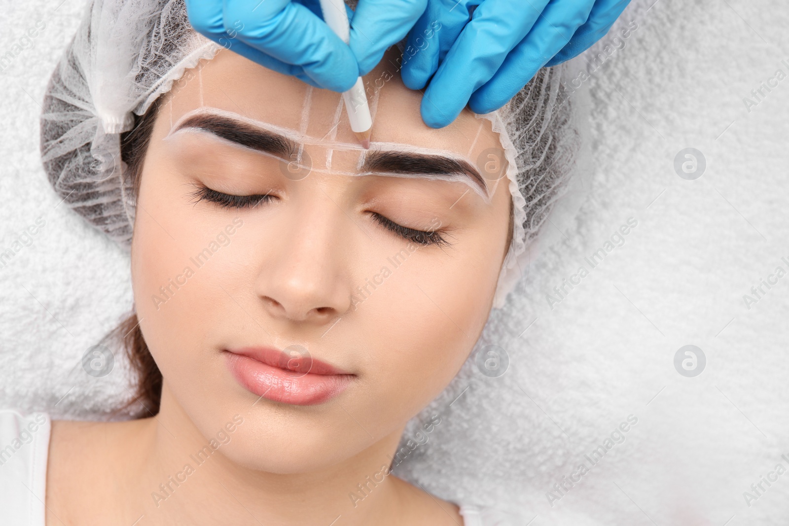 Photo of Cosmetologist preparing young woman for eyebrow permanent makeup procedure, closeup