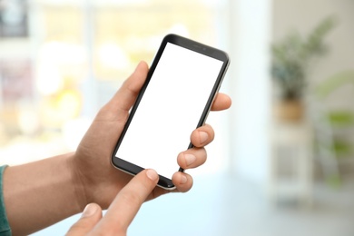 Photo of Man holding smartphone with blank screen indoors, closeup of hands. Space for text