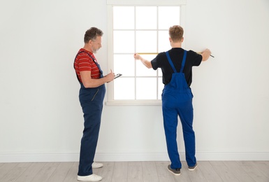 Service men measuring window for installation indoors