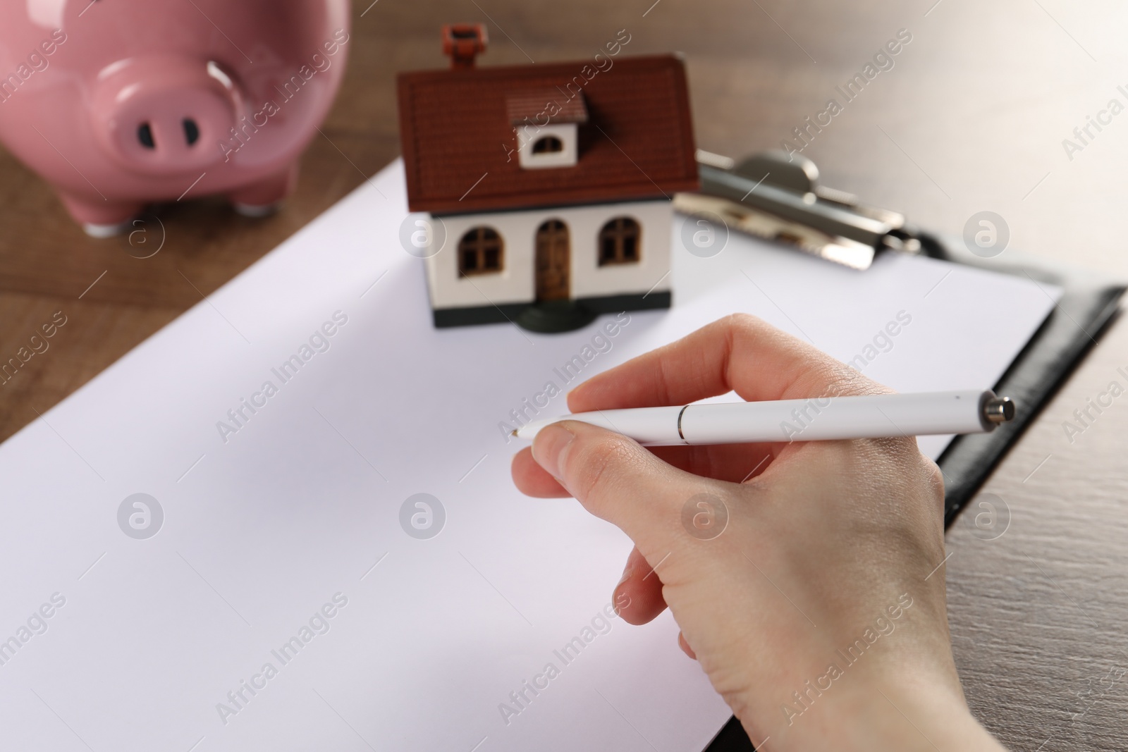 Photo of Woman planning budget, closeup. House model and piggy bank on wooden table