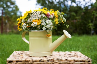 Photo of Pale yellow watering can with beautiful flowers on wicker box outdoors