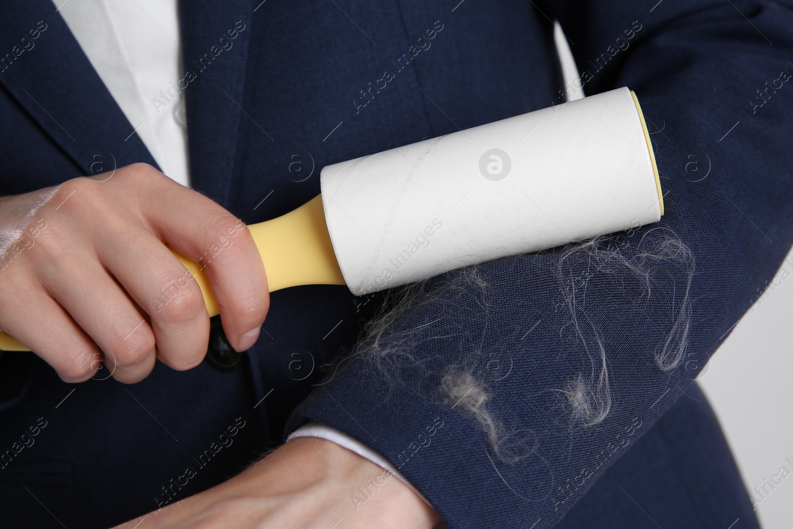 Photo of Woman removing cat hair from dark blue jacket with lint roller, closeup