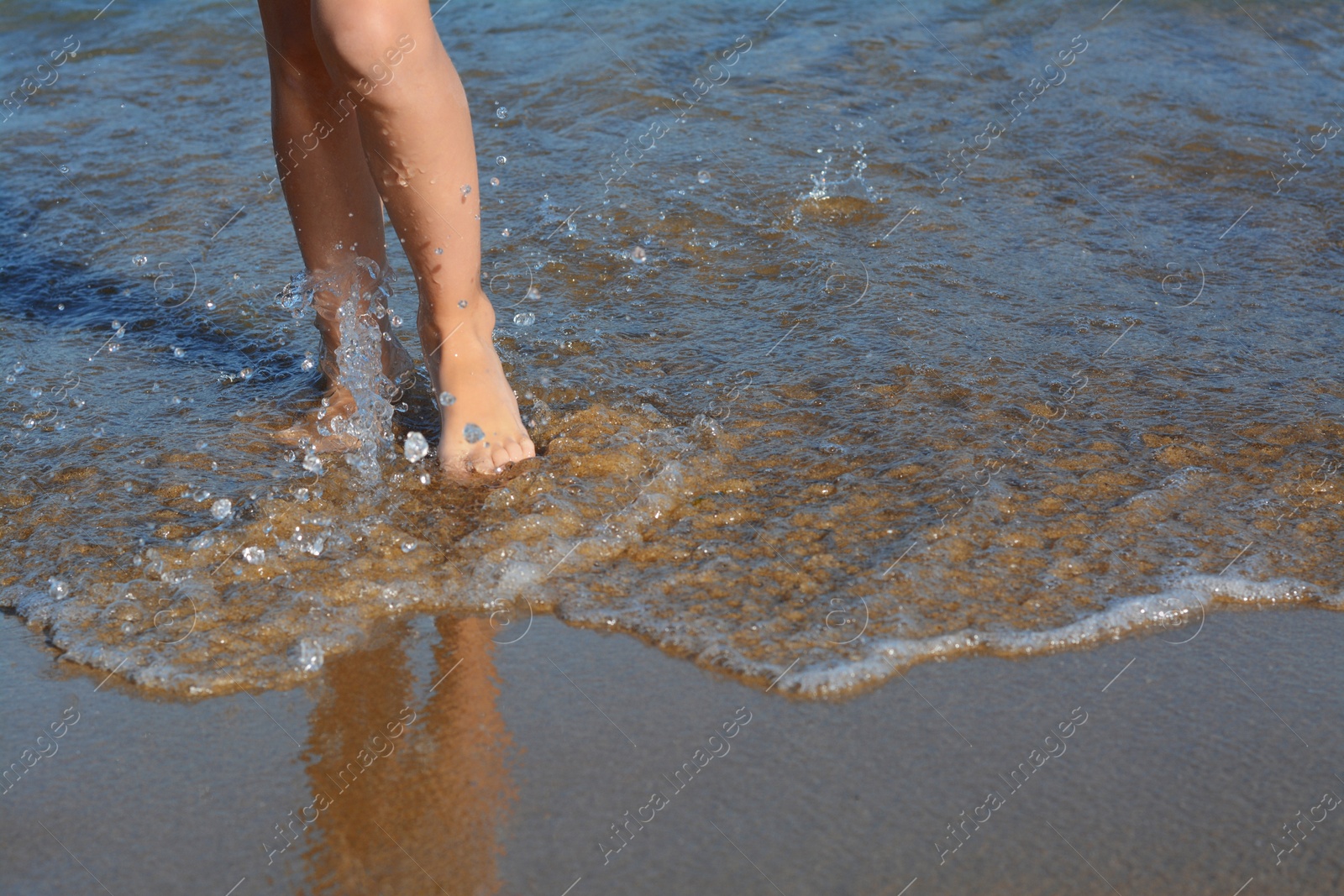 Photo of Child walking through water on seashore, closeup of legs. Space for text