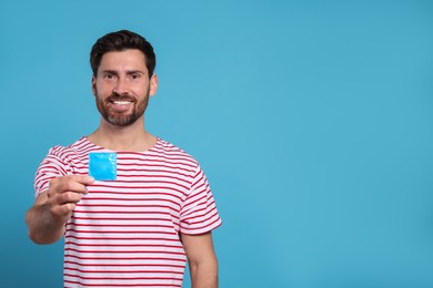 Happy man holding condom on light blue background, space for text. Safe sex