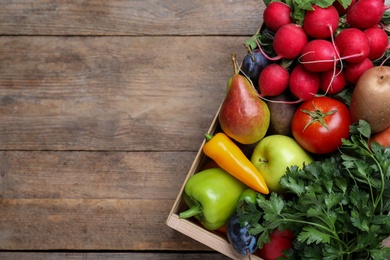 Crate full of harvested vegetables and fruits on wooden table, top view. Space for text