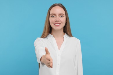 Photo of Happy young woman welcoming and offering handshake on light blue background