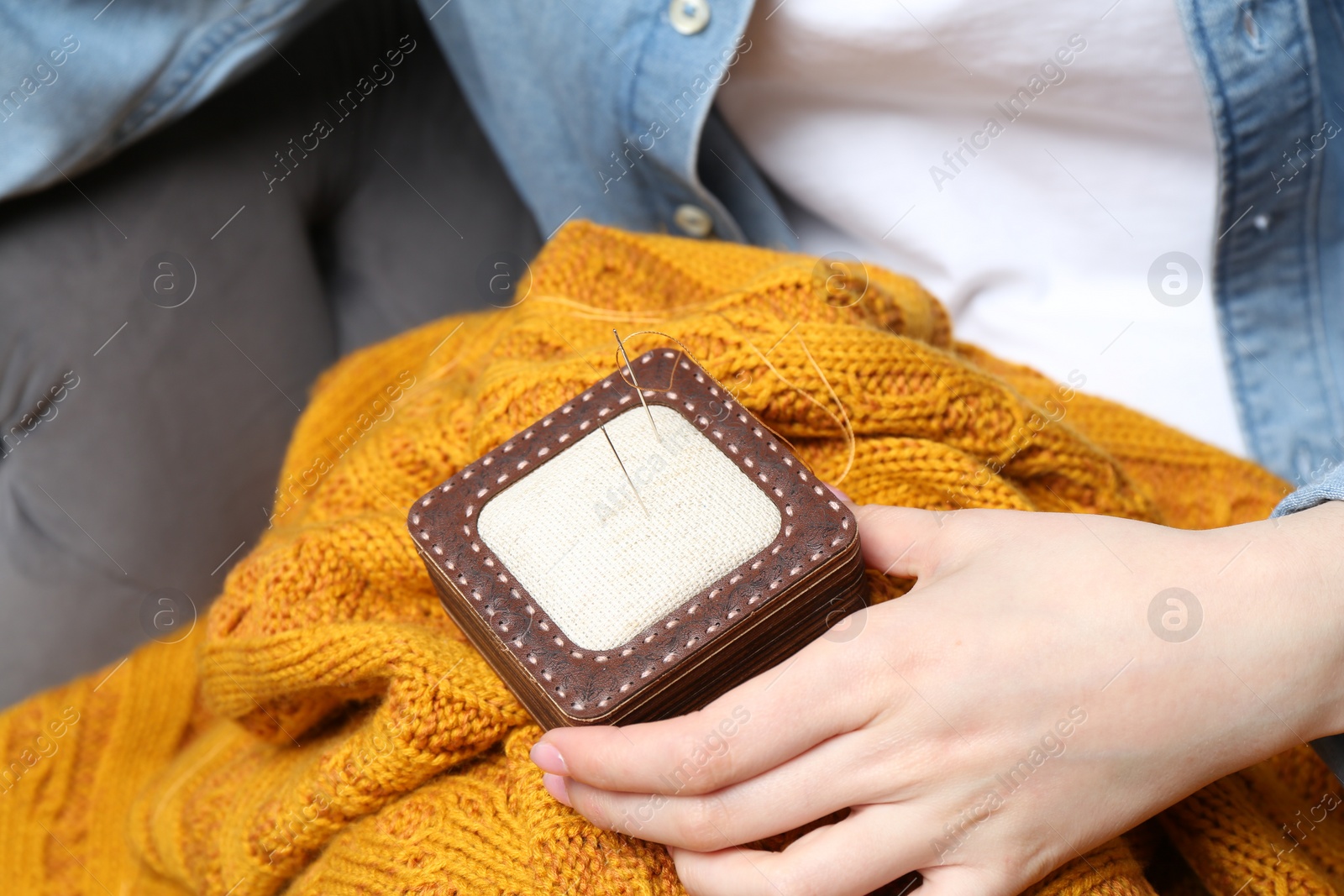 Photo of Woman holding pin cushion with sewing needles and sweater, closeup