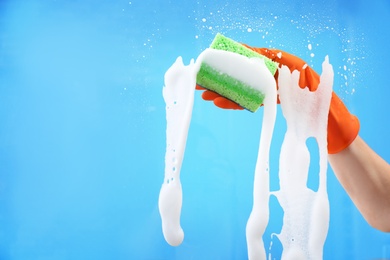 Photo of Woman cleaning glass with sponge against color background