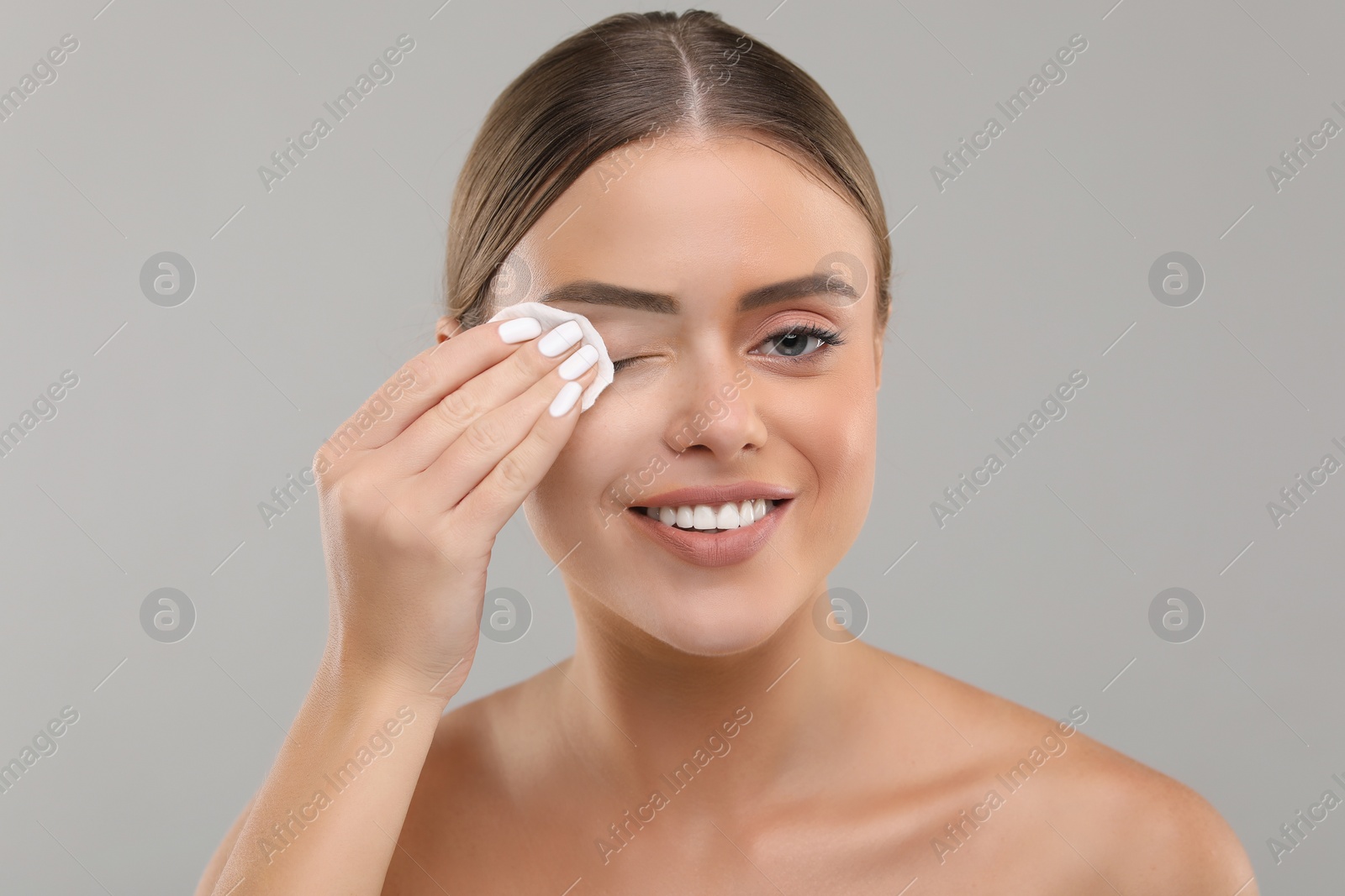 Photo of Beautiful woman removing makeup with cotton pad on grey background