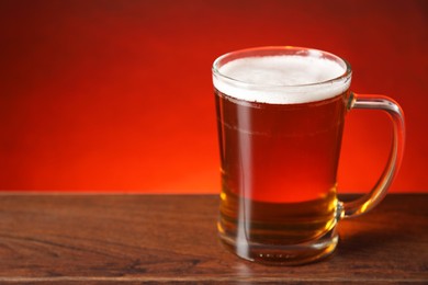Photo of Mug with fresh beer on wooden table against red background. Space for text