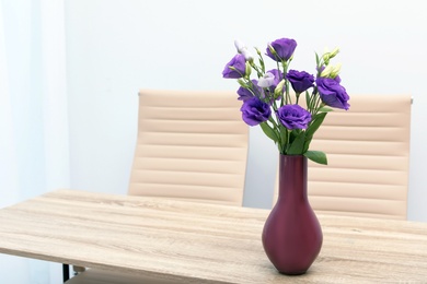 Photo of Beautiful bouquet in vase on wooden table against color background. Stylish interior