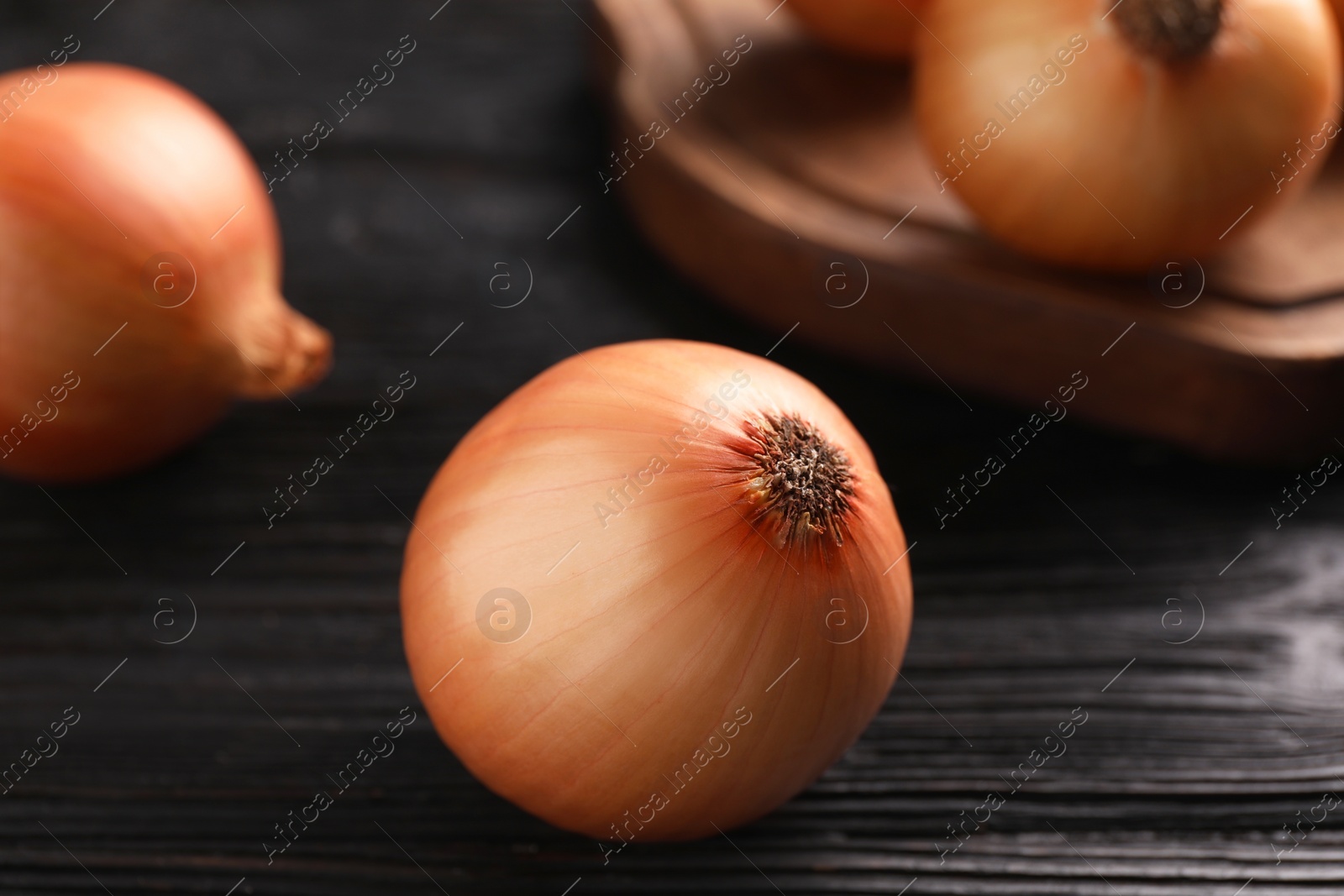 Photo of Ripe onions on black wooden table, closeup