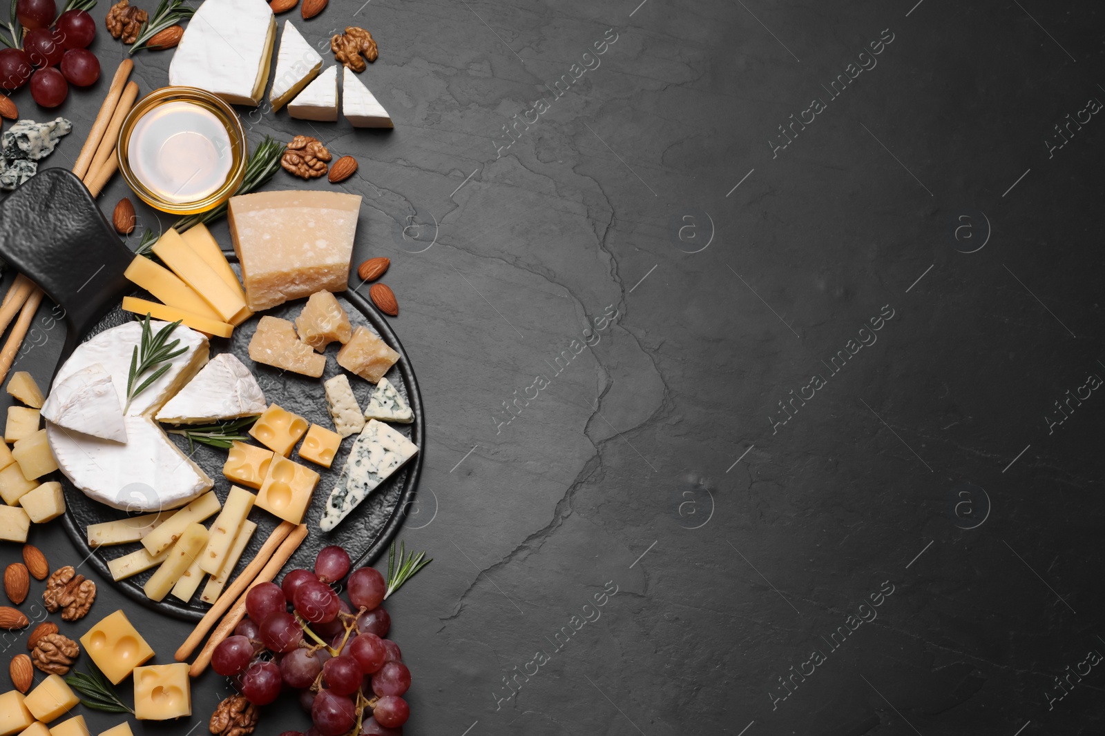 Photo of Cheese plate with honey, grapes and nuts on black table, flat lay. Space for text