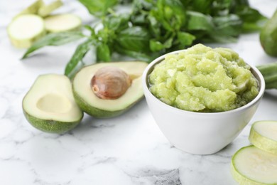 Photo of Bowl with tasty puree, zucchini, avocado and basil on white marble table