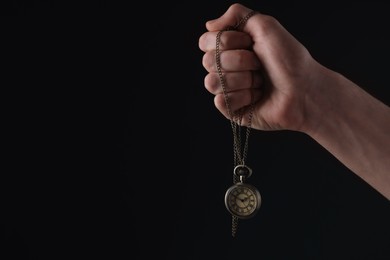 Man holding chain with elegant pocket watch on black background, closeup. Space for text