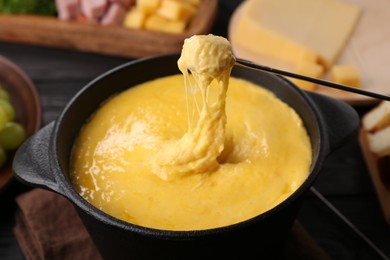 Dipping piece of ham into fondue pot with melted cheese on table, closeup