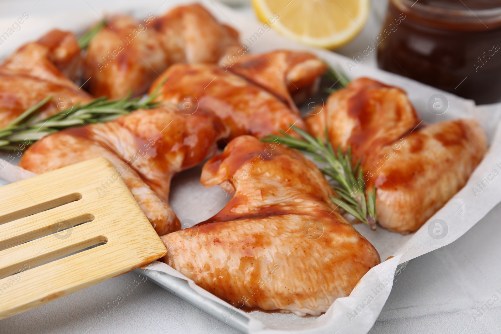 Photo of Raw marinated chicken wings, rosemary and spatula on light tiled table, closeup