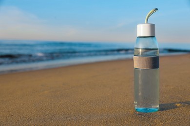 Photo of Glass bottle with water on wet sand near sea. Space for text