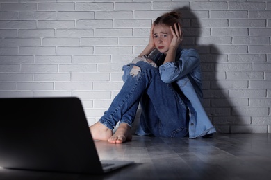 Scared teenage girl with laptop on floor in dark room. Danger of internet