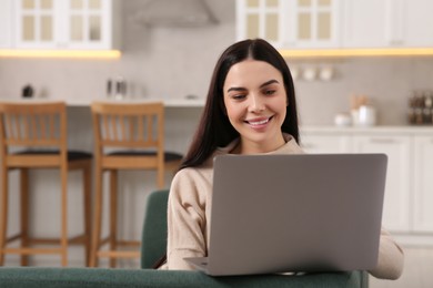 Photo of Happy woman working with laptop on sofa in kitchen
