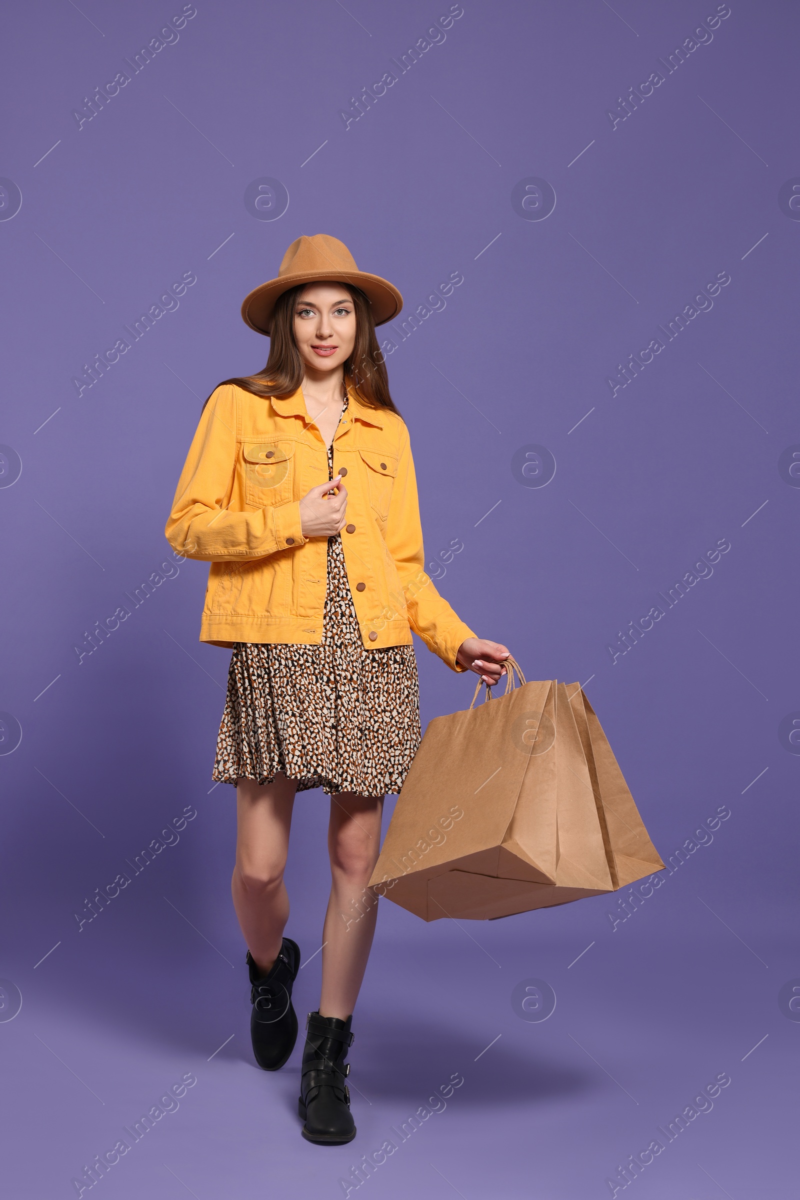 Photo of Stylish young woman with shopping bags on purple background