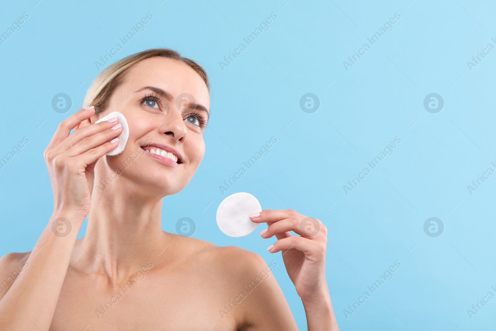 Photo of Smiling woman removing makeup with cotton pads on light blue background. Space for text