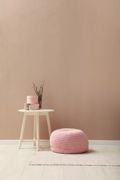 Knitted pouf and decor elements near beige wall indoors. Space for text