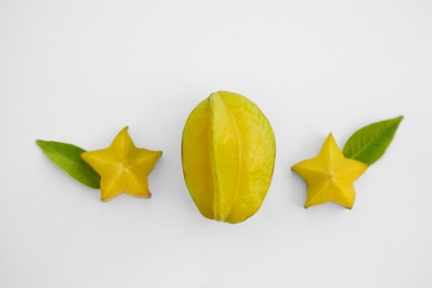 Delicious cut and whole carambolas with green leaves on white background, top view