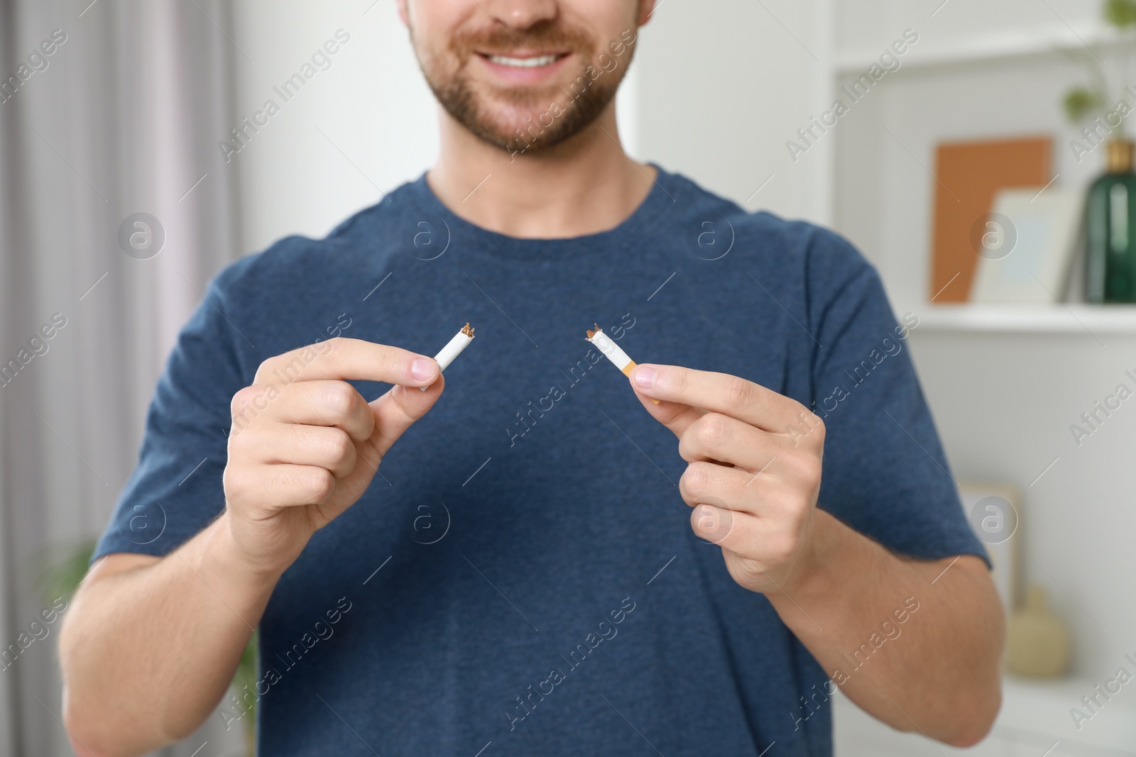 Photo of Stop smoking concept. Man holding pieces of broken cigarette at home, closeup