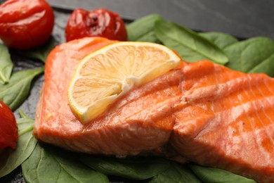 Tasty grilled salmon with tomatoes, lemon and spinach on table, closeup