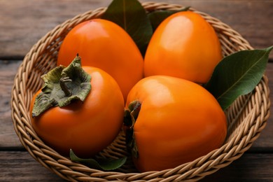 Photo of Delicious ripe persimmons in wicker basket on wooden table, closeup
