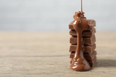 Photo of Pouring tasty milk chocolate paste onto pieces on wooden table, closeup. Space for text