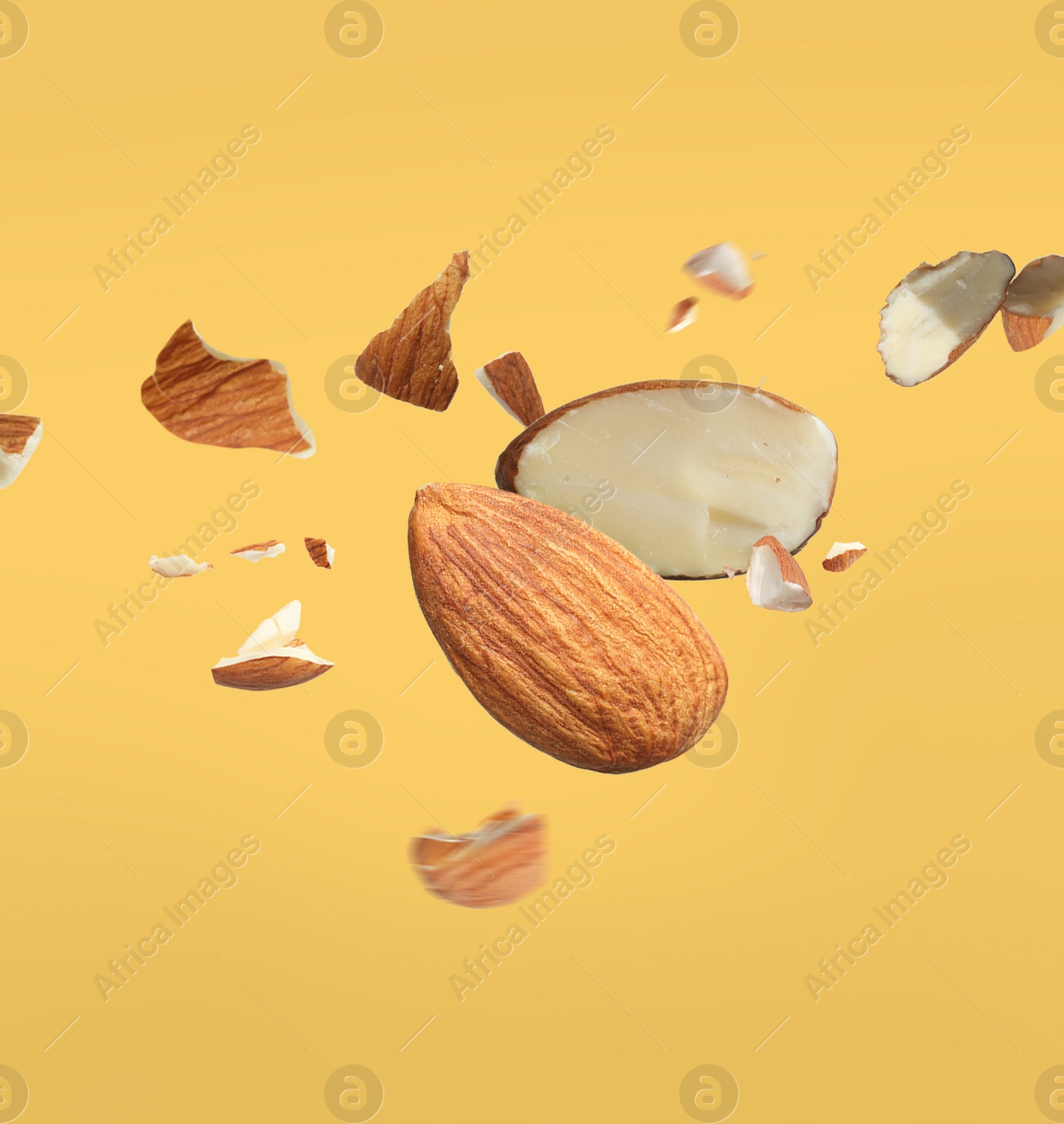 Image of Pieces of tasty almonds falling on yellow background