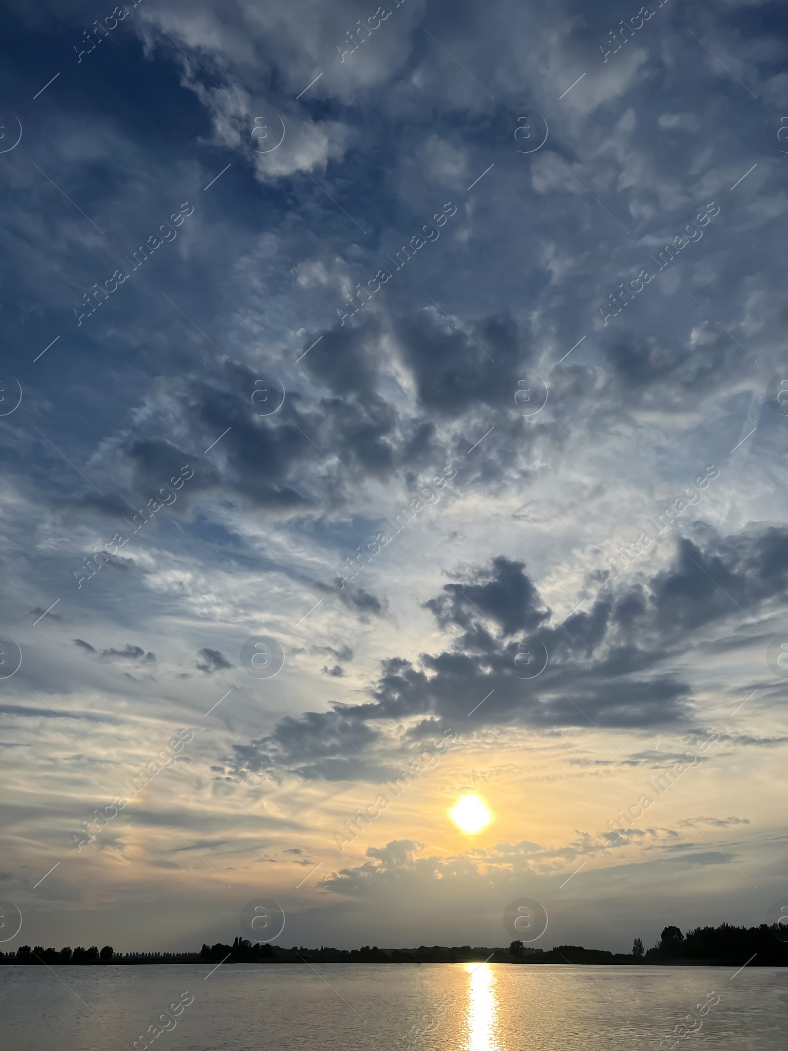 Photo of Sun in cloudy sky over lake during sunset