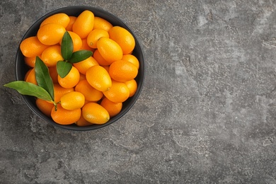 Photo of Fresh ripe kumquats in bowl on grey table, top view. Space for text