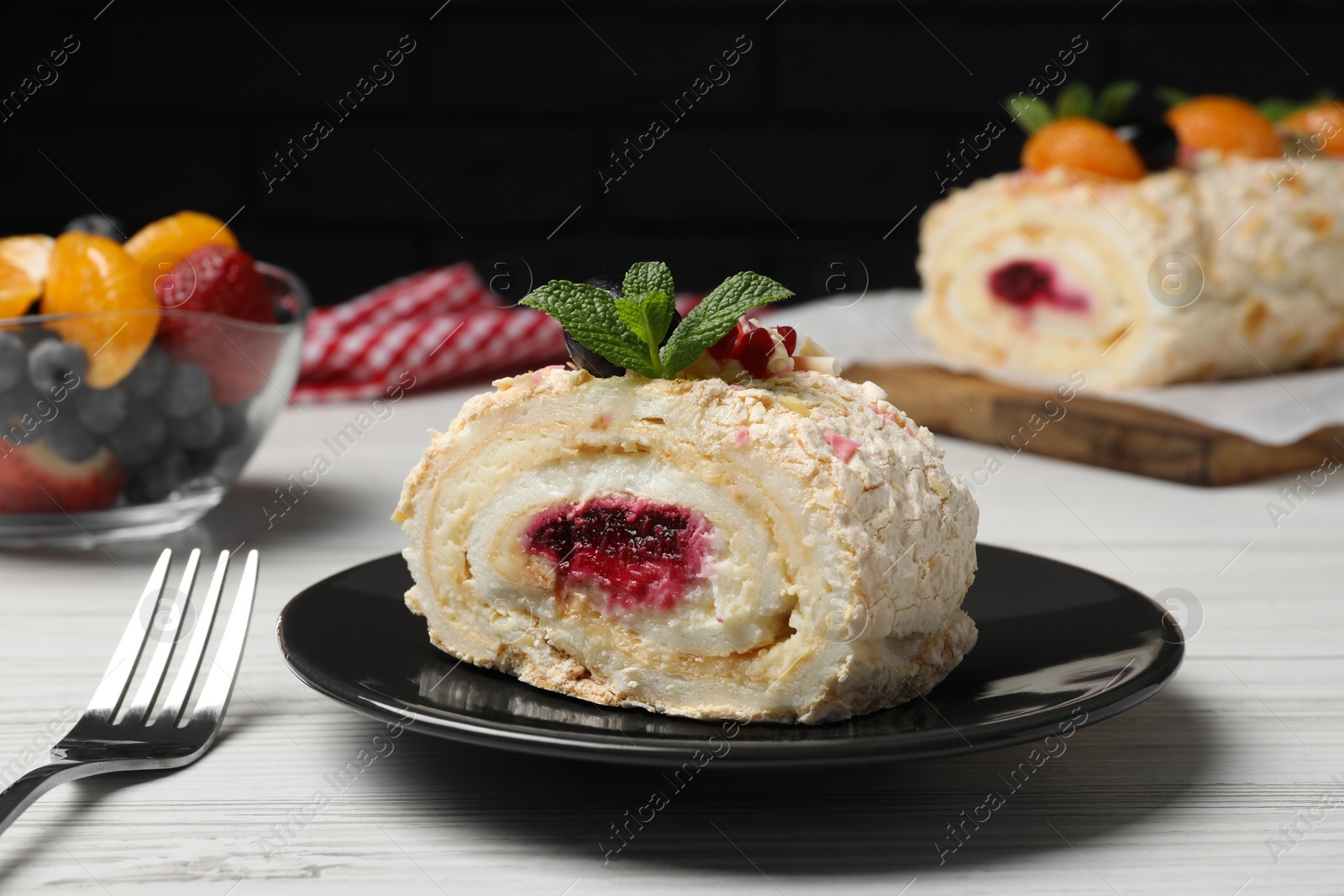 Photo of Slice of tasty meringue roll with jam and mint leaves on white wooden table, closeup