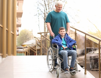 Preteen boy in wheelchair with his grandfather using ramp outdoors