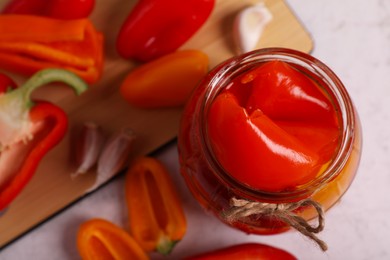 Photo of Jar with tasty pickled peppers and fresh vegetables on table, closeup. Space for text