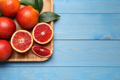 Photo of Whole and cut red oranges on light blue wooden table. Space for text