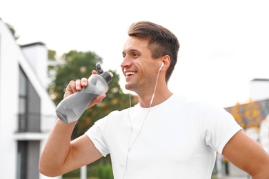 Photo of Young man with earphones drinking water after running on street. Healthy lifestyle